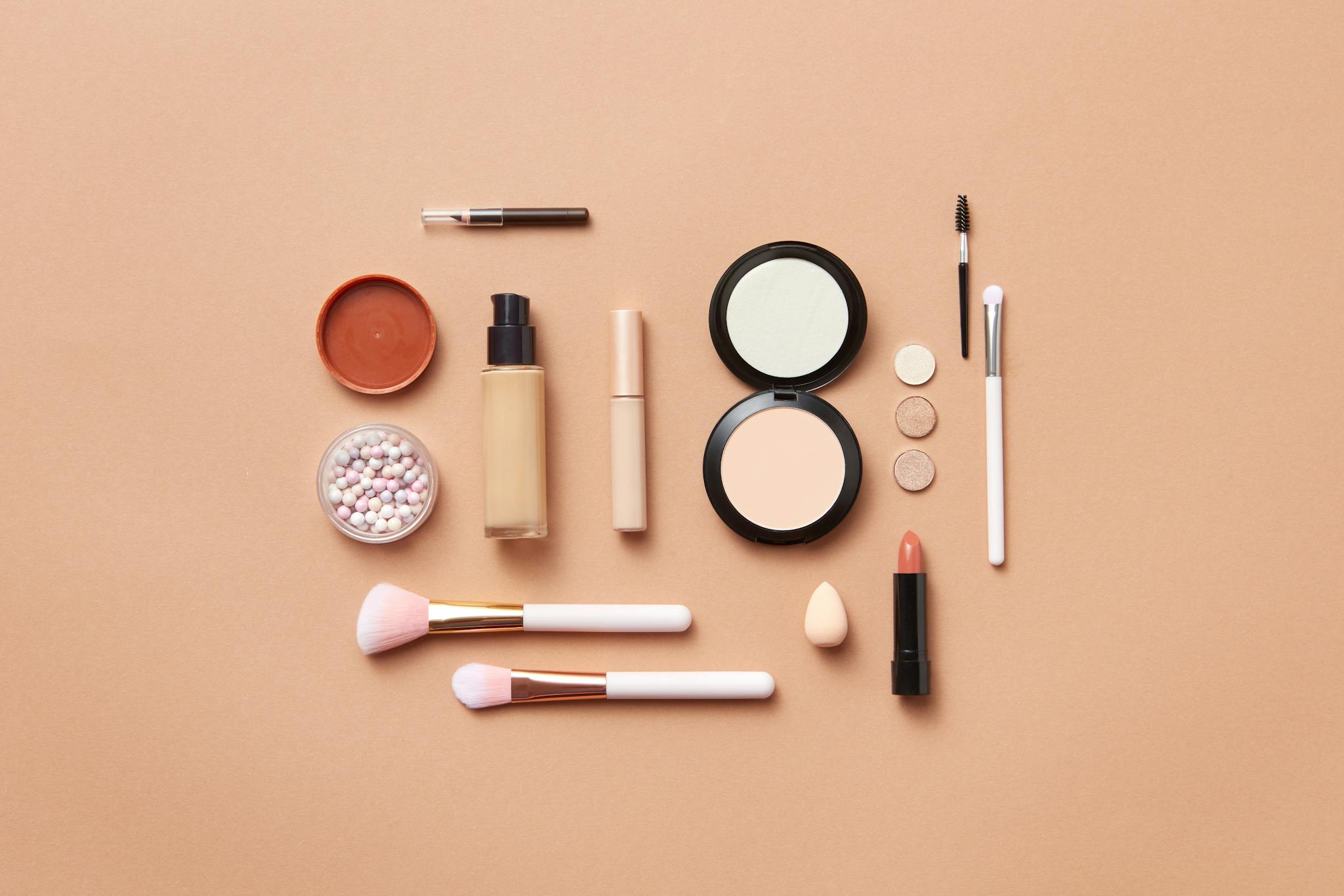 Stylish flatlay of various makeup products on a soft peach background.