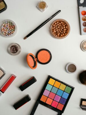 A vibrant collection of makeup and beauty products arranged in a flat lay on a white background.