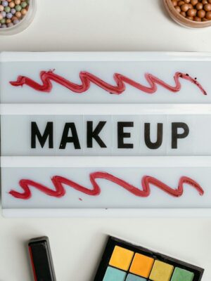 Flat lay of makeup items with lipstick, powder, and palette surrounding a sign reading 'MAKEUP'.
